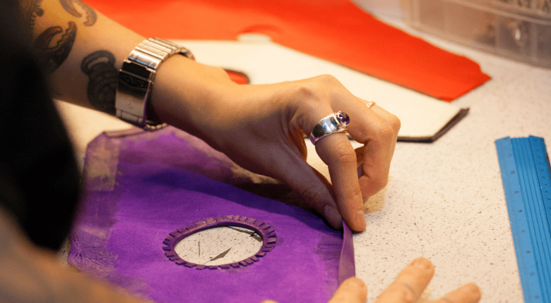 A close-up of a person hand-glueing a purple leather thigh harness