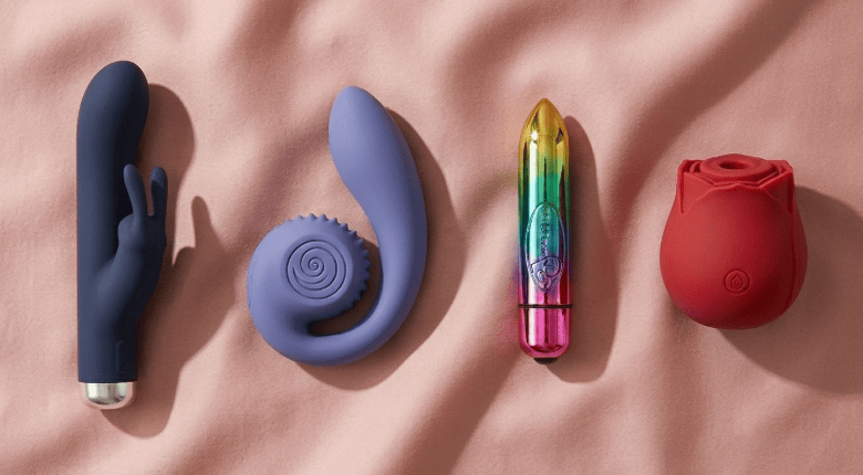 Four silicone sex toys in different colors on a pink fabric background