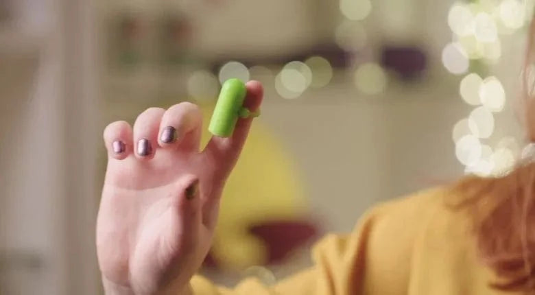 Close-up of a small finger vibrator on someones hand with warm blurry lighs in the. background.