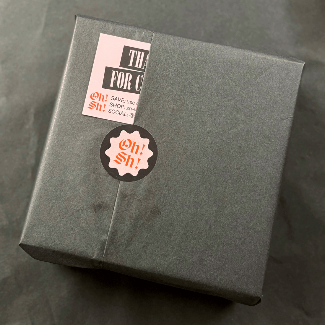 Gray gift box with 'Oh! Sh!' label on a dark surface