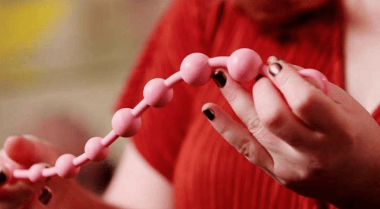 A close-up of a person holding a string of pink silicone anal beads.