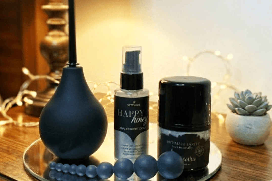 Black anal douche, black latex gloves & 2 anal enhancer creams displayed on a mirror with fairy lights