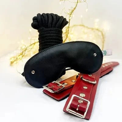 Black leather blindfold and red leather restraints on a white background with decorative lights.