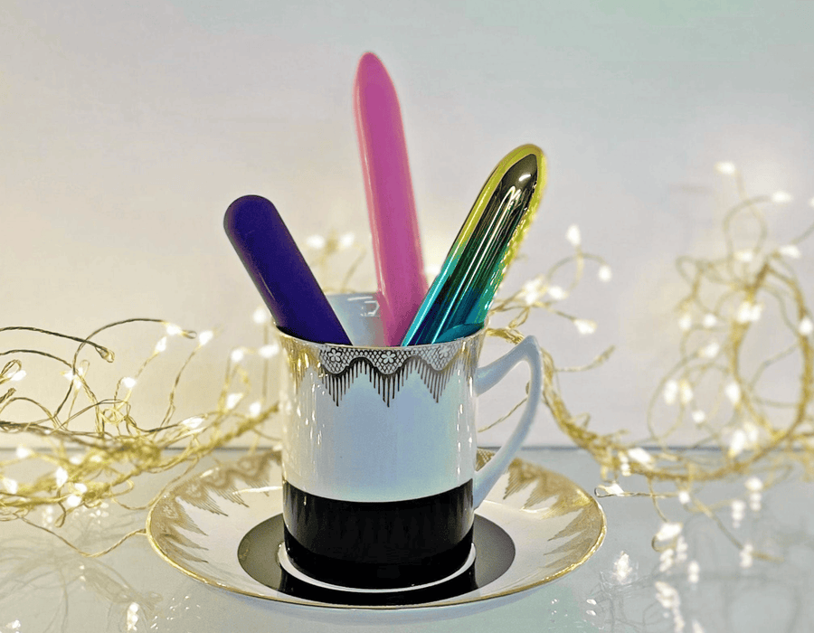 Three colorful bullet vibrators in a elegant cup and saucer, with softly-lit  background with warm fairy lights.