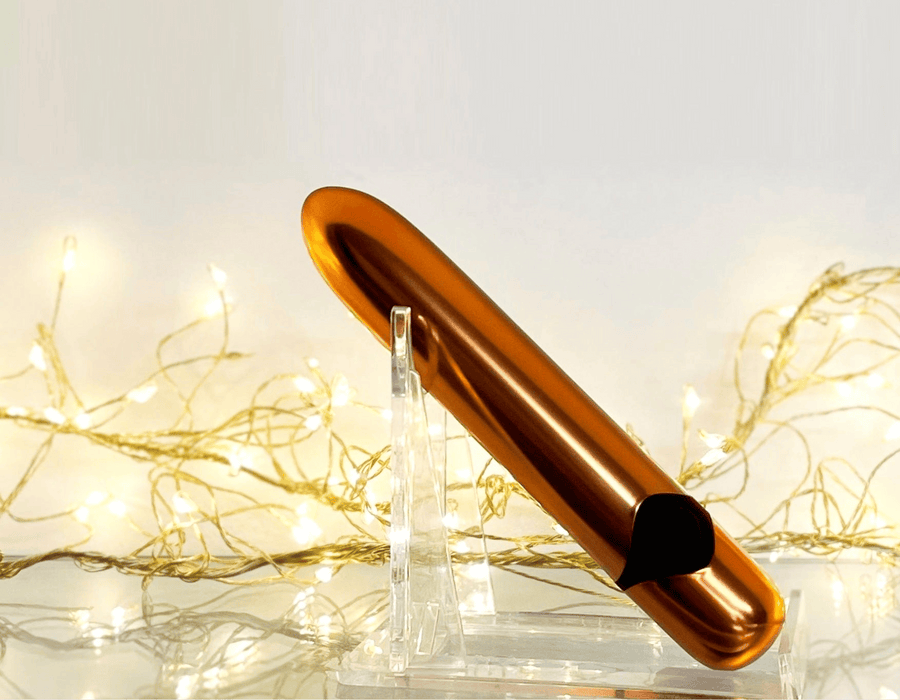Gold classic bullet vibrator on a clear stand with string lights in the background