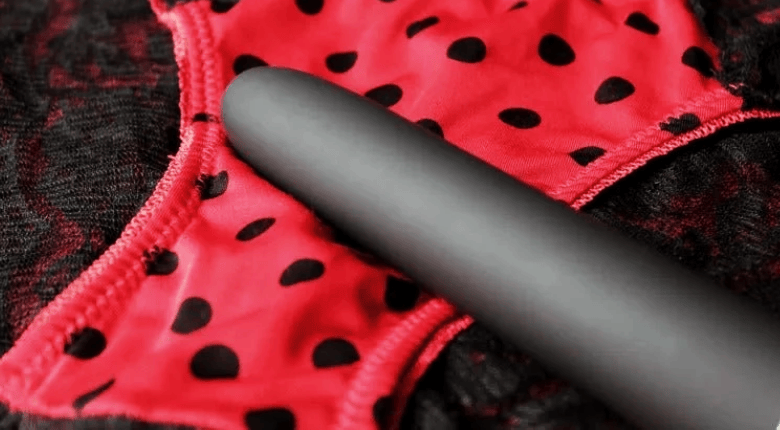 Close-up of a black classic, smooth vibrator resting on red and black polka-dot underwear.