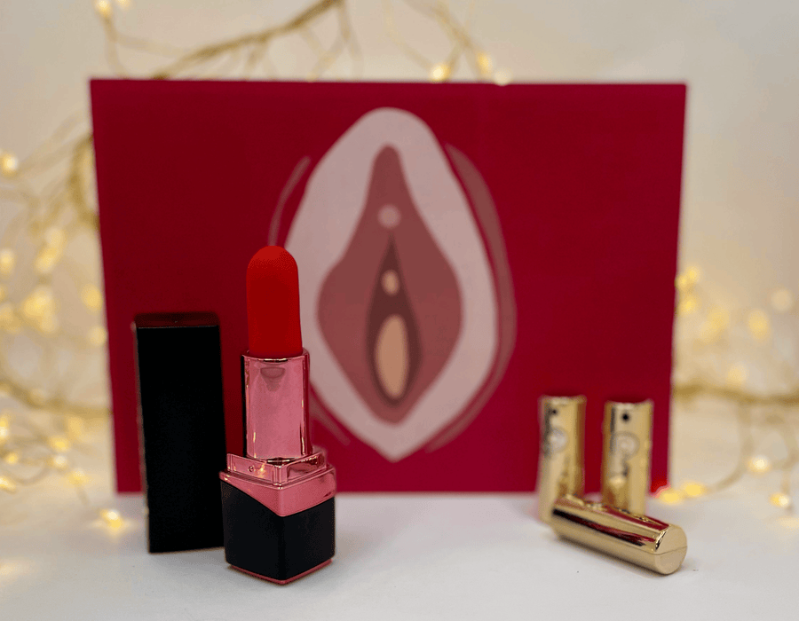 A red lipstick vibrator & gold bullet vibrators in front of a red card featuring a stylized vulva graphic.