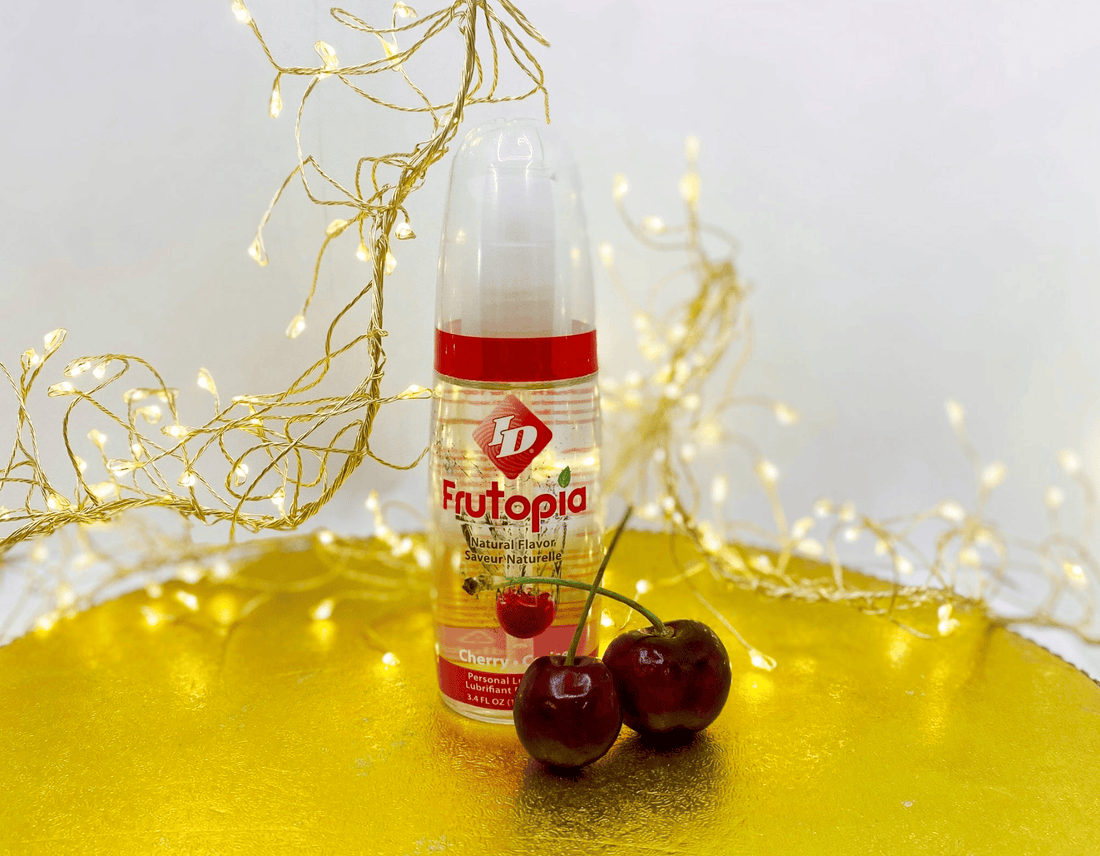 A bottle of Frutopia cherry-flavored syrup or juice stands on a reflective gold surface with two fresh cherries in front.