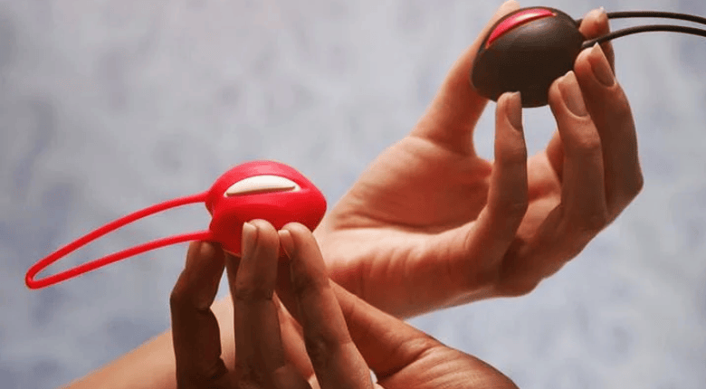 Two hands holding single kegal balls against a soft gray background.