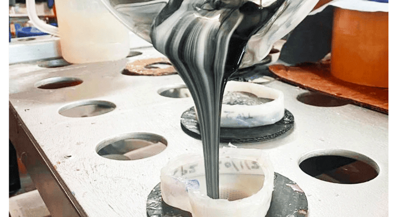 A close-up shot of a jug pouring marbled black & white silicone into a dildo mould