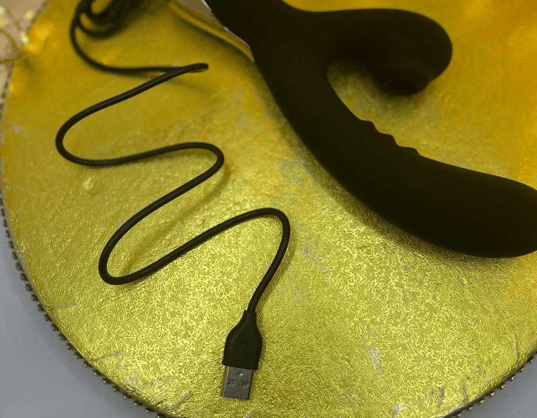 Black USB charging cable connected to a black vibrator, laid on a textured gold circular board.