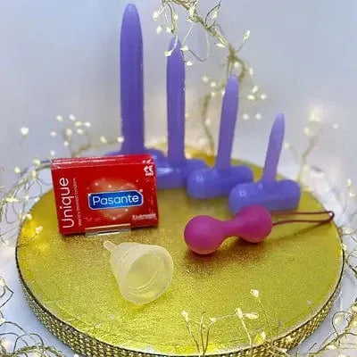 A set of sexual wellbeing products arranged on a round gold tray, including purple silicone vaginal dilators, pink kegal balls, a mooncup,and a red box of condoms