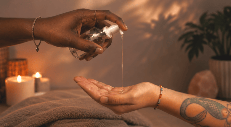 A clear pump bottle dispensing a thin stream of  silicone lube onto an open palm, with a second hand holding the bottle.