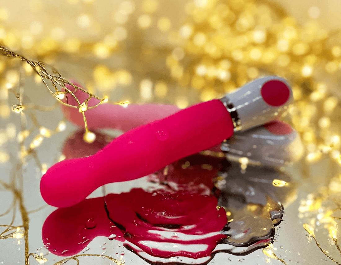 A pink waterprrof vibrator, resting on a reflective surface in a puddle of water.